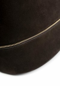 Borsa in suede marrone scuro con una texture liscia, caratterizzata da una cerniera dorata lungo il bordo e un design con base arrotondata.