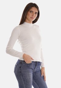 Maglietta a maniche lunghe bianca con collo alto in tessuto morbido, design aderente, con dettagli a coste sul colletto e sull'orlo, abbinata a jeans blu scuro.