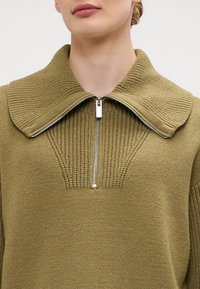 Suéter de malha verde-oliva com gola com fecho éclair, apresentando um relevo texturizado e um decote amplo. Costura detalhada na área do peito.