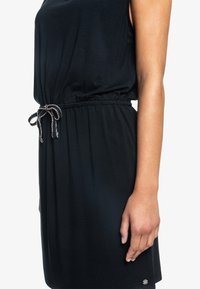 Vestido negro con un corte relajado, cintura elástica con cordón, tejido suave y un pequeño detalle de logo en el dobladillo.