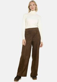 Brązowe zamszowe spodnie typu wide-leg z wysokim stanem, z przednimi zaszewkami. Połączone z białym golfem i brązowymi butami sportowymi.