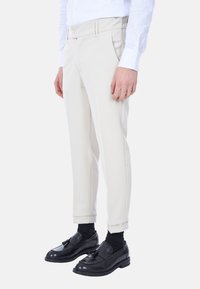 Pantaloni bianchi su misura realizzati in tessuto leggero, con vestibilità slim, tasche frontali e chiusura con bottone in vita, abbinati a scarpe nere.