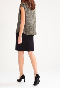 Metallinen, teksturoitu lyhythihainen paita hopeanvärisenä, joka on yhdistetty mustaan polvipituiseen hameeseen ja mustiin korkeakorkoisiin kenkiin.