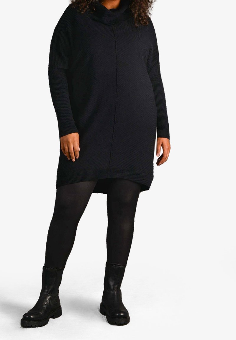 Abito tunica nero in maglia con collo a sciarpa, maniche lunghe e texture a coste, abbinato a collant neri e stivali alla caviglia.