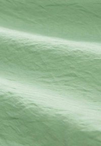 Tejido en un suave color verde menta con una textura arrugada. La tela parece ligera y suave, mostrando sutiles variaciones en el tono.