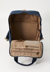 Navy blue backpack with a zippered tan compartment. Interior is lined with a smooth, brown fabric. Features dual handles and storage pockets.