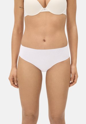 Mujer con bragas de algodón blancas simples y un sujetador blanco, de pie con los brazos relajados a los lados sobre un fondo neutro.