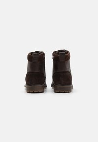 Botines marrones que combinan cuero liso y ante, con un cuello acanalado y suela de goma texturizada. Cremalleras laterales para un fácil acceso.