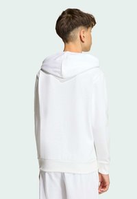 Biela mikina s kapucňou a klokanie vrecko s rebrovanými manžetami. Mäkká textúra a minimalistický dizajn s voľným strihom.