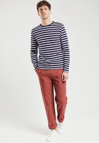 Marineblå og hvide stribede langærmede skjorte parret med røde chinos og hvide sneakers. Fokuser på en afslappet pasform og markant farvekontrast.