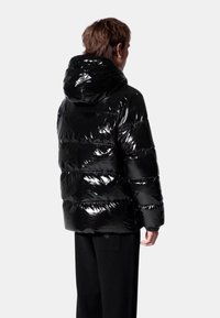 Veste noire rembourrée avec une finition brillante, dotée d'une capuche et d'un design matelassé horizontal. Portée avec un pantalon noir, vue de dos.