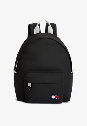Sac à dos noir Tommy Jeans avec poche zippée frontale et détail de poignée blanche sur fond blanc uni.