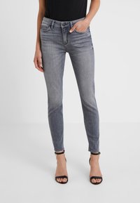Jeans gris de corte slim con cinco bolsillos, cierre de botón y un leve acabado desgastado. Combinados con sandalias negras de tacón.