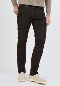 Czarne zamszowe dżinsy o slim fit, z pięcioma kieszeniami, metalowym zapięciem i subtelną strukturą, zestawione z jasnymi butami.