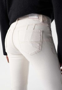 Slim-fit, high-waisted jeans in light beige denim with back pockets, subtle stitching details, and a label at the waistband.