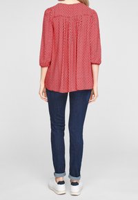 Blouse à motifs rouges avec des manches trois-quarts, détail froncé au dos, associée à un jean bleu foncé et des baskets blanches avec des accents marine.