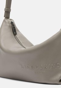 Borsa in pelle grigia dal design morbido, chiusura con zip, logo impressa e tracolla regolabile. Superficie liscia, stile minimalista e forma curvata.