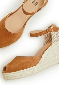 Sandalias de cuña de ante marrón con punta abierta, correa en el tobillo y detalles de tela trenzada. Suela estilo rafia para mayor textura y agarre.