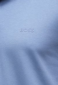 Ανοιχτό μπλε ύφασμα με ανάγλυφα τονικά γράμματα "BOSS" στο κέντρο.