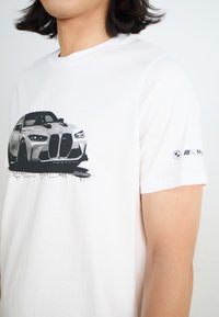 Biała bawełniana koszulka z krótkim rękawem z czarnym nadrukiem samochodu na przodzie oraz logo BMW nadrukowanym na rękawie. Slim fit z okrągłym dekoltem.