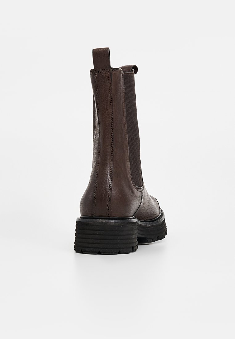 Schokoladenbraune Leder-Stiefeletten mit elastischen Seitenpaneelen, einer strukturierten Ferse und einer gerippten schwarzen Sohle für besseren Halt. Sichtbare verstärkte Nahtdetails.
