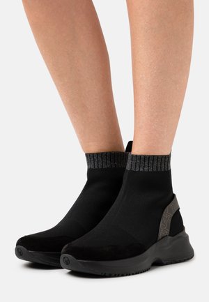 Černé kotníkové boty ve stylu ponožek s texturovaným žebrovaným lemem a semišovými detaily. Mají zakřivenou, polstrovanou podrážku pro pohodlí.