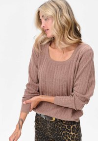 Bruine geribbelde trui met een brede halslijn en losse mouwen, gecombineerd met een broek met dierenprint. Glad textuur, ontspannen pasvorm.