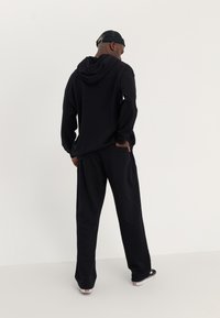 Haut à capuche noir avec cordon de serrage et poche kangourou, associé à un pantalon de survêtement assorti. Tissu doux, coupe décontractée et design minimaliste.