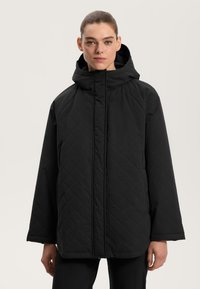 Črna, quiltana puffer jakna s kapuco. Ima ravno krojenje, dolge rokave in sprednji zadrgo. Mat tekstura, minimalističen oblikovanje.