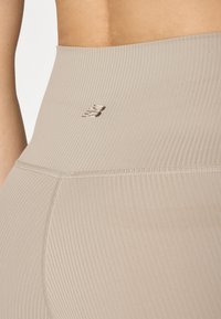 Leggings de sport beige avec une texture côtelée et un petit logo brodé sur la taille. Dotés de coutures plates pour le confort.