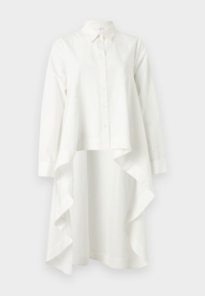 Μακρύ λευκό πουκάμισο-φόρεμα με μακριά μανίκια, κουμπιά μπροστά, μυτερό γιακά και ασύμμετρο βολάν στο τελείωμα.