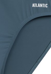 Niebieskie majtki kąpielowe wykonane z gładkiego syntetycznego materiału, z wycięciem w wysokim stylu i białym napisem logo "ATLANTIC" po boku.