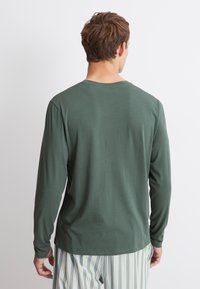 Donkergroene blouse met lange mouwen, gemaakt van zachte stof, met een ronde hals en een licht ontspannen pasvorm, gecombineerd met lichtgestreepte broek.