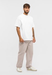 Biela bavlnená tričko s voľným strihom, kombinované so svetlo béžovými nohavicami s širokými nohavicami. Model má na sebe biele tenisky s jemným logom.