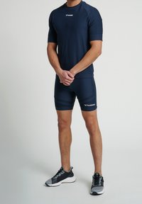 Granatowa koszulka sportowa i dopasowane spodenki, wykonane z materiału odprowadzającego wilgoć, z subtelną teksturą i akcentami logo. Buty sportowe w kolorze szarym.