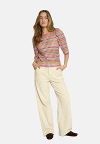 Fitted, multicolored patterned top with three-quarter sleeves. Paired with wide, off-white trousers and dark brown footwear.