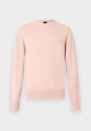 Pull rose clair à manches longues avec col rond, poignets et ourlet côtelés, avec un petit patch logo discret sur la poitrine gauche.