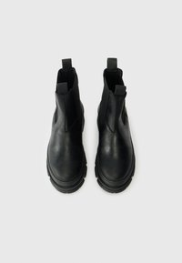 Bottines en cuir noir à tige mi-mollet avec des panneaux latéraux élastiques, bout rond et semelles en caoutchouc épaisses. Comprend des languettes pour un enfilage facile.