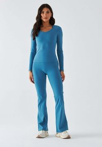Niebieski top z długim rękawem w zestawie z dopasowanymi, rozszerzanymi spodniami do jogi. Wykonany z gładkiego materiału, o dopasowanym kroju i dekoltem w łódkę.