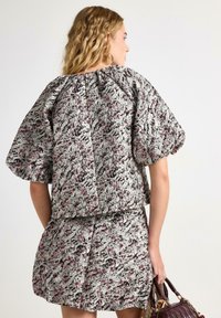 Lyhythihainen, lyhyt toppi ja sen kanssa yhteensopiva hame, jossa on kuviollinen kangas, joka sisältää harmaan, vaaleanpunaisen ja mustan sävyjä. Pintatekstuurissa on hieman kiiltävä viimeistely.