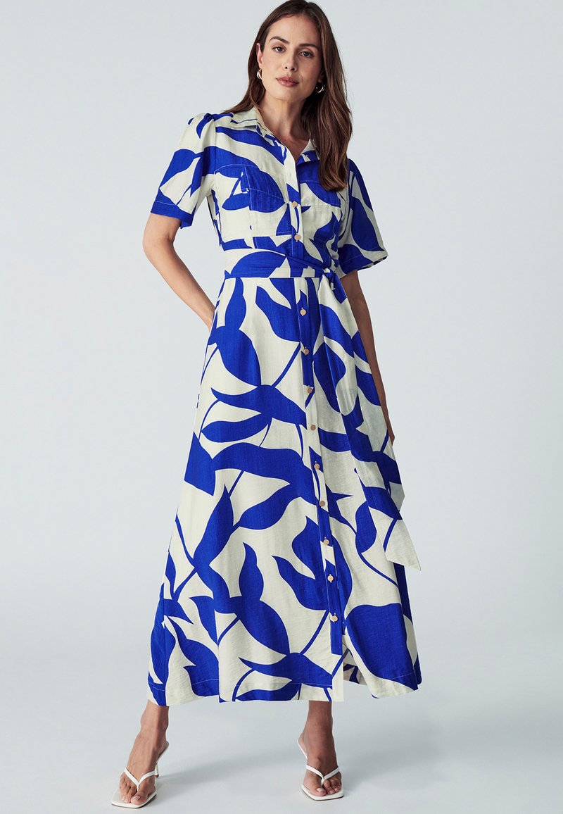 Maxi šaty v modré a krémové barvě s květinovým vzorem, krátkými rukávy, zapínáním na knoflíky vpředu a páskem na zavázání, vyrobené z lehkého materiálu.