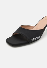 Fekete nyitott orrú papucs, pamutból készült, széles pánttal, amelyen fehér "LOVE MOSCHINO" felirat található, és rövid, tömb sarkával.