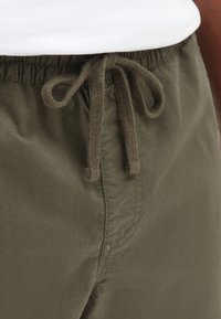 Olivenfarvede shorts med elastisk talje og snor. Har blødt stof og synlige sømme langs siderne.
