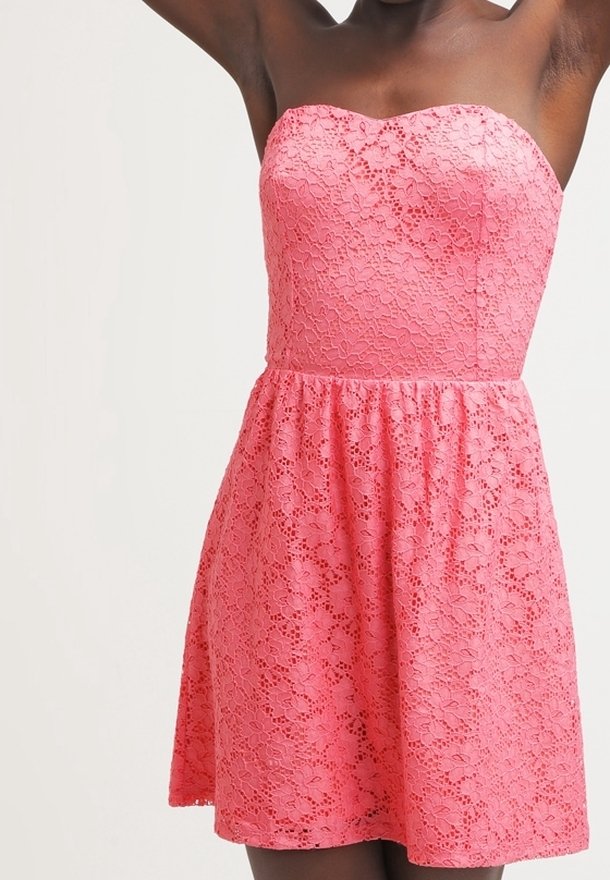 Robe bustier rose en dentelle avec motif floral, corsage ajusté et jupe évasée portée par une personne aux bras levés sur un fond uni.