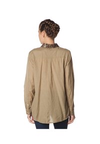 Camisa de manga larga, color marrón claro, con un cuello estampado, confeccionada con una tela texturizada. Presenta un corte relajado y un pliegue en la parte trasera para mayor comodidad.