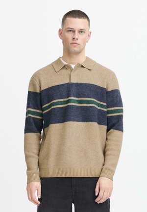 Pull en tricot beige avec des motifs rayés bleu marine et vert, dotée d'un col et d'une fermeture éclair mi-haut, en tissu texturé et avec des poignets côtelés.