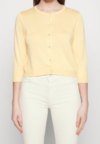 Lys gul cardigan med rund halsudskæring, 3/4 ærmer og frontknaplukning. Lavet af blødt materiale, har en almindelig pasform.