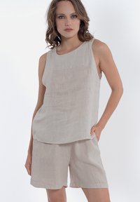 Beige linnen mouwloze top gecombineerd met bijpassende shorts. Eenvoudig, los ontwerp met een gladde textuur en minimale details.