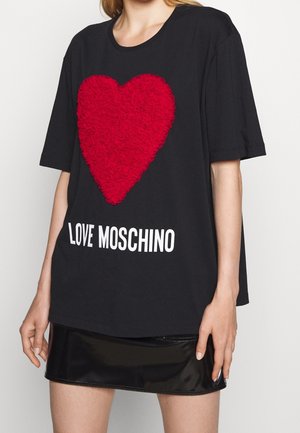 Kobieta nosząca czarny oversize t-shirt z dużym teksturowanym czerwonym sercem i białym tekstem "LOVE MOSCHINO", zestawiona z czarną spódnicą.