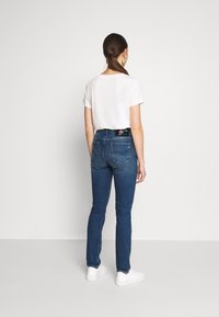 Bílý top s krátkým rukávem, kombinovaný s tmavě modrými skinny džíny. Džíny mají pásek s květinovým vzorem a zadní kapsy s viditelným švem.